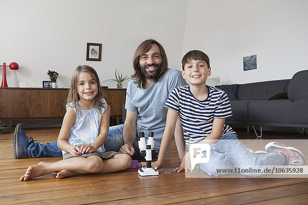 Porträt von Vater und Kindern mit Mikroskop auf dem Boden zu Hause sitzend