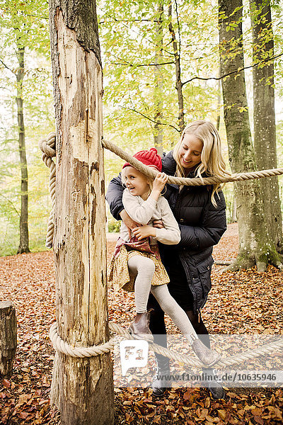 Glückliche Mutter  die ihrer Tochter beim Balancieren auf einem Seil im Wald hilft