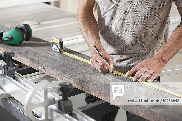 Midsection of male carpenter measuring plank on sliding table saw in workshop