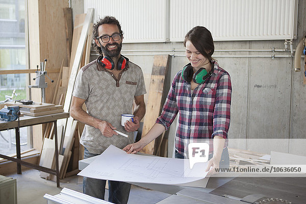 Laughing male and female carpenters with blueprint in workshop