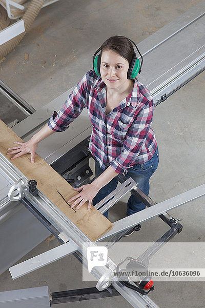 High angle portrait of happy female carpenter using a sliding table saw in workshop