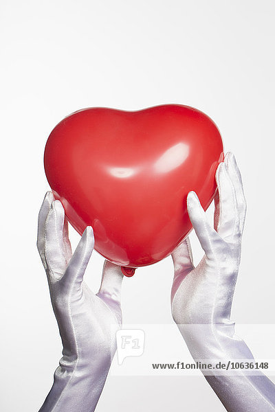 Cropped hands of bride holding heart shape balloon against white background