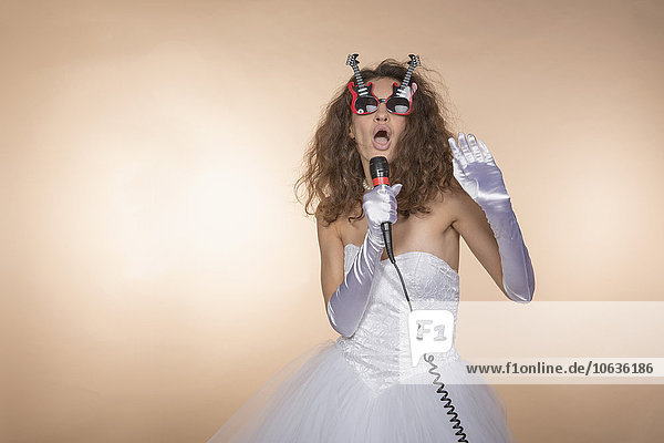 Excited bride in guitar shaped glasses singing against colored background
