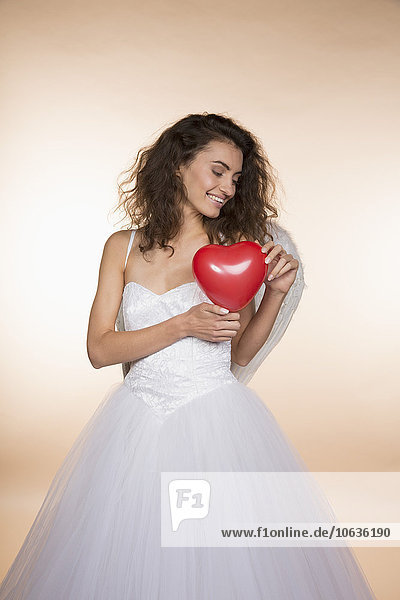 Happy bride holding heart shape balloon against colored background