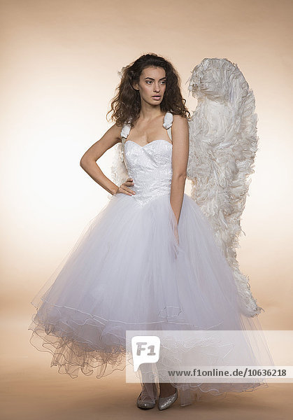 Confident bride in angel wings standing against colored background