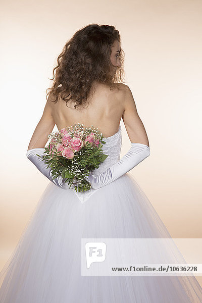 Rear view of bride holding bouquet against colored background
