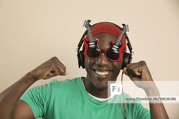 Porträt eines fröhlichen jungen Mannes mit gitarrenförmiger Brille und Kopfhörer