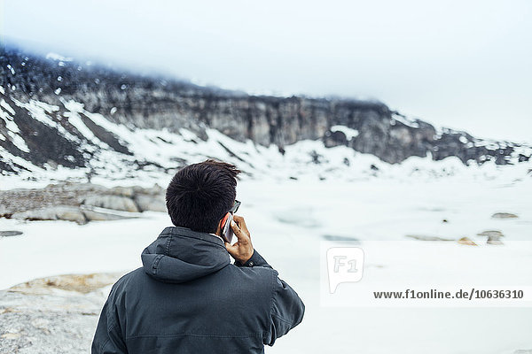 Rear view of man using mobile phone on snow covered field