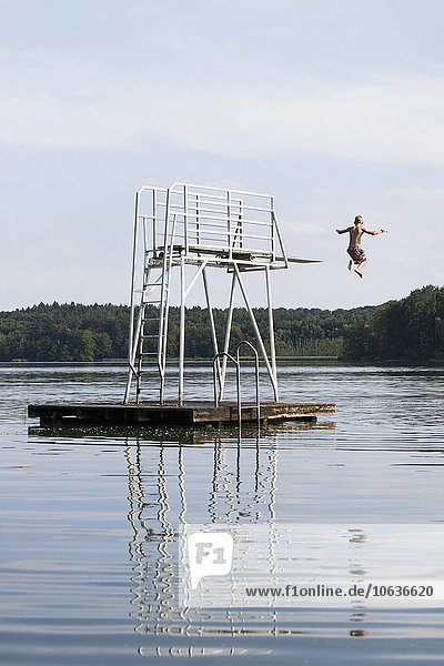 Rear view of boy jumping in lake against sky