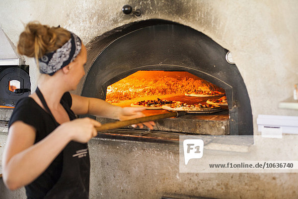 Köchin legt Pizza in den Holzofen
