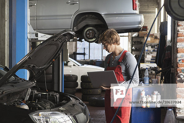 Mechaniker mit Laptop bei der Untersuchung des Fahrzeugmotors in der Werkstatt