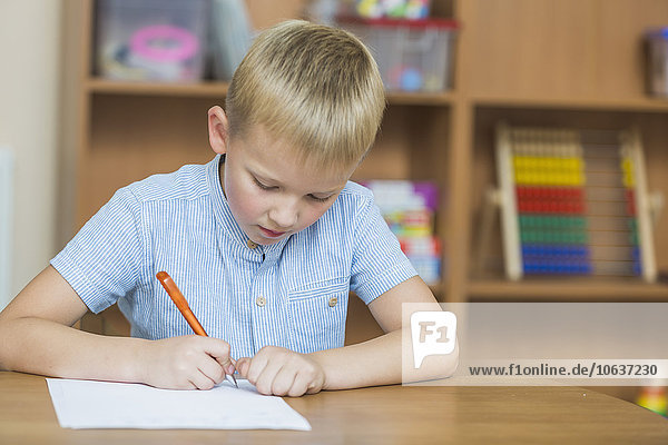 Konzentrierter Junge beim Schreiben auf Papier am Tisch