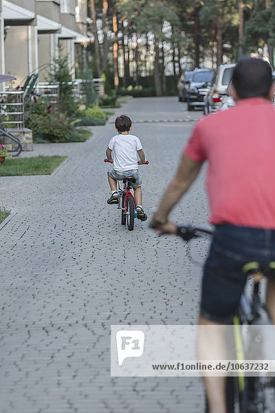 Rear view of father and son riding bicycle on street