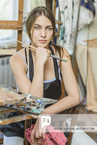 Porträt einer schönen Malerin  die im Atelier auf einem Stuhl sitzt.