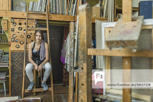 Künstlerin sitzend auf Leiter im Atelier