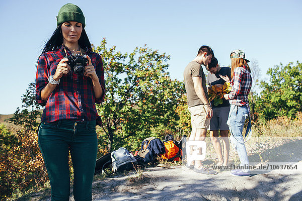 Young woman looking at photographs on camera with friends standing in forest