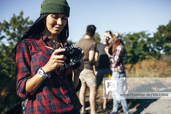 Young woman looking at photographs on camera with friends standing in forest