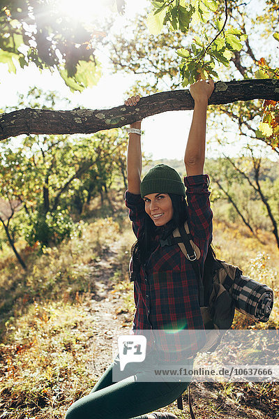 Portrait of smiling woman swinging from branch in forest
