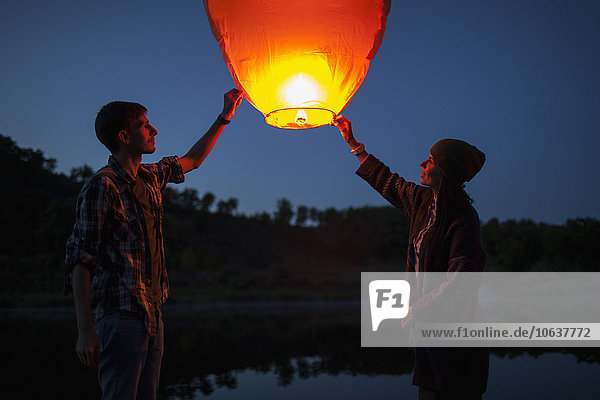 Man and woman releasing paper lanterns at lakeshore