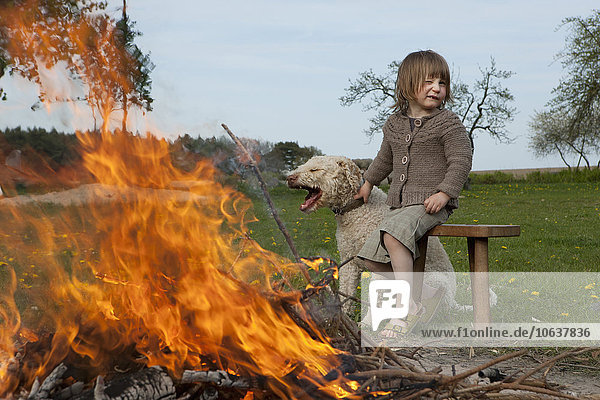 Girl and dog sitting by bonfire on field