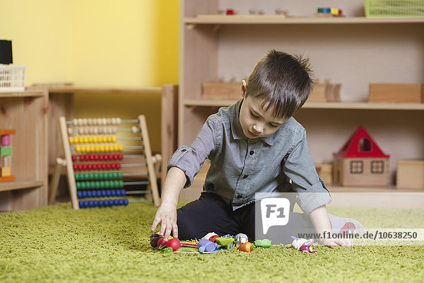 Volle Länge des Jungen  der mit Spielzeug auf dem Teppich im Klassenzimmer spielt.