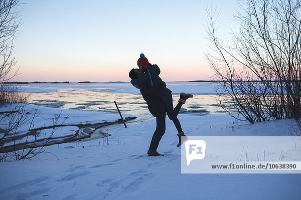 Full length of young man picking up woman and kissing on snow covered field