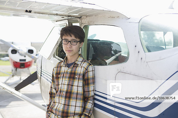 Porträt eines selbstbewussten Teenagers  der vor einem Privatflugzeug steht.