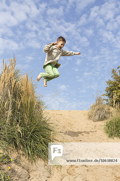 Junge springt auf Sanddüne gegen den Himmel