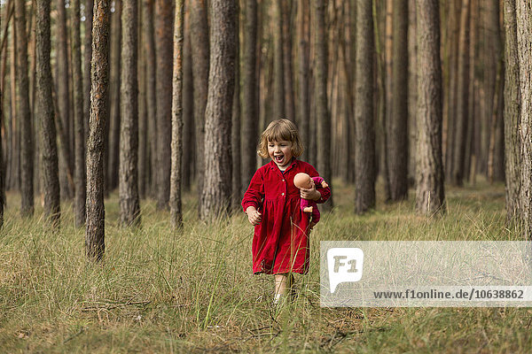 Glückliches Mädchen hält Puppe beim Waldspaziergang