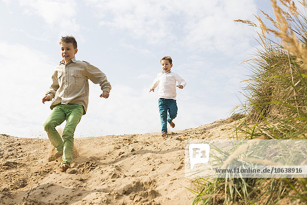 Low angle view of brothers running on sand dune