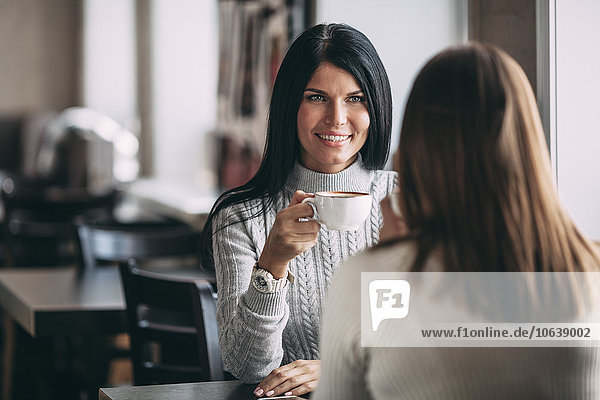 Happy young woman having coffee with female friend in cafe