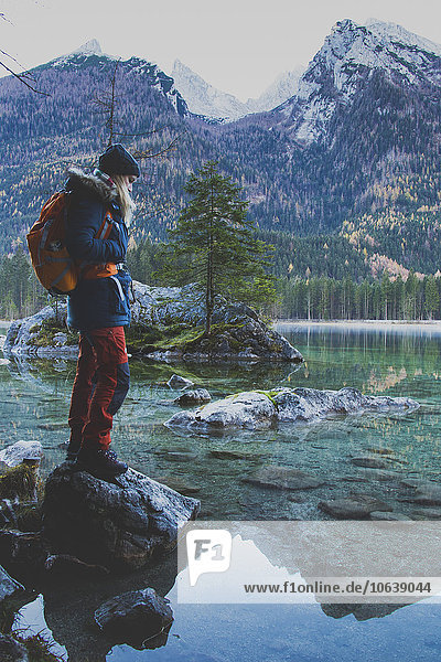 Seitenansicht einer Wanderin  die am Hintersee auf einem Felsen gegen die Berge steht.