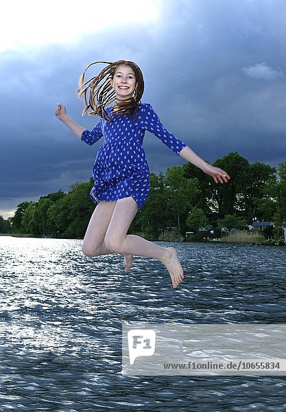Girl jumping into water with dress on  dark clouds  Ellbogensee  Upper Havel  Priepert  Mecklenburg Lake District  Mecklenburg-Western Pomerania  Germany  Europe