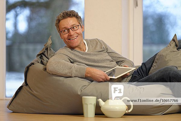 Mann liegt auf einem großen Kissen mit Tablet PC  eBook  iPad  tablet computer  Deutschland  Europa
