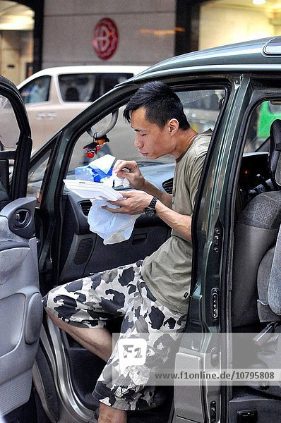 Hong Kong: a man eating in his car  in Central                                                                                                                                                          .