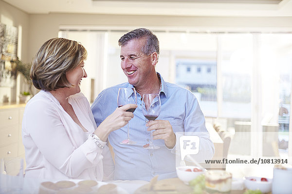 Smiling couple toasting red wine glasses in kitchen