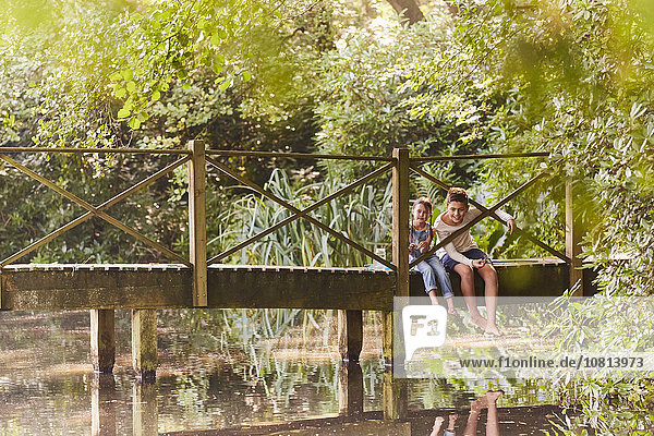 Bruder und Schwester sitzen auf einer Fußgängerbrücke im Park mit Bäumen.
