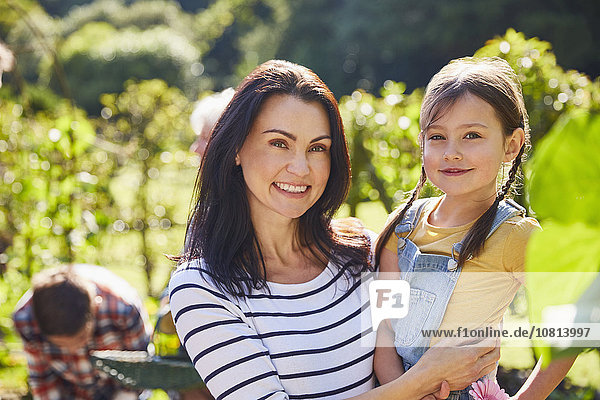 Portrait lächelnde Mutter und Tochter umarmend im sonnigen Garten