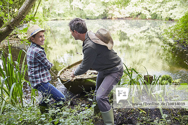 Vater und Sohn ziehen Boot an Land im Teich