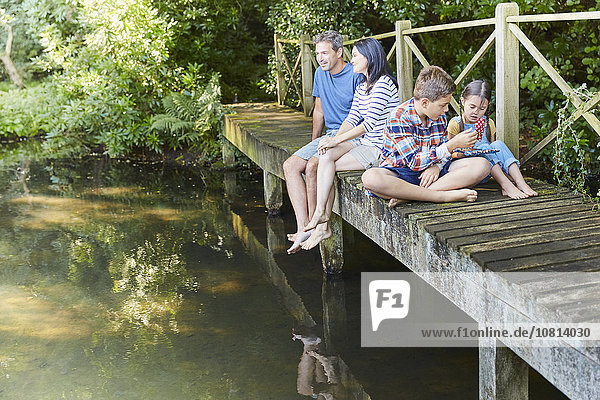 Family relaxing on footbridge over pond
