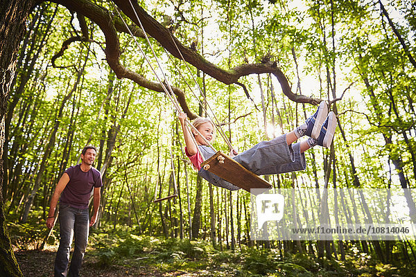 Father pushing daughter on rope swing in forest