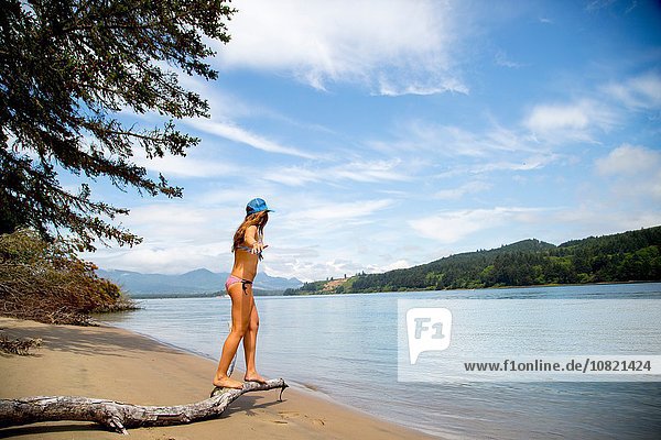 Young woman wearing bikini balancing on tree branch at beach  Nehalem Bay  Oregon  USA