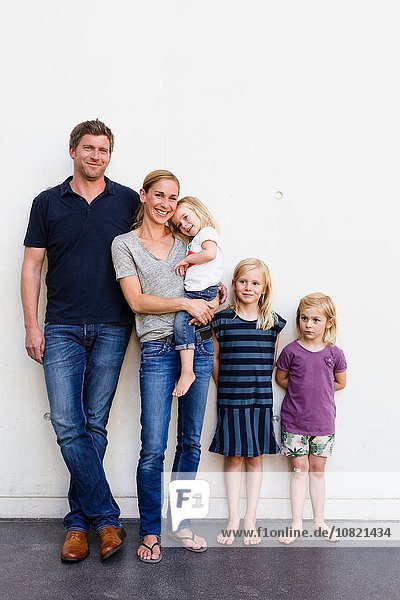 Porträt von Eltern und drei jungen Töchtern  die vor der weißen Wand stehen