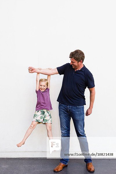 Porträt eines reifen Mannes mit einer Tochter  die vor einer weißen Wand am Arm hängt.