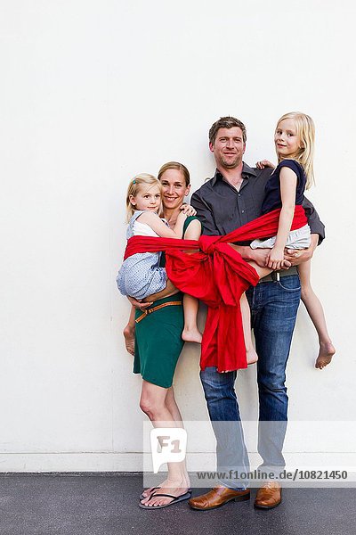 Porträt von Eltern und zwei Töchtern in rotem Band vor der weißen Wand
