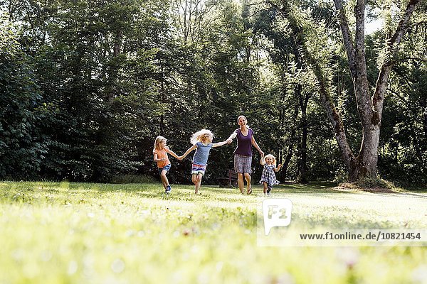 Mid adult woman and three young daughters holding hands and running in park