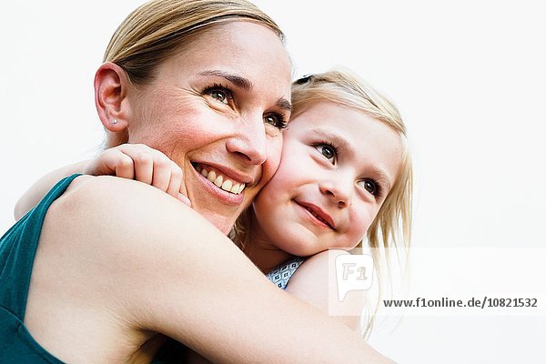 Portrait of mid adult woman and daughter hugging in front of white wall