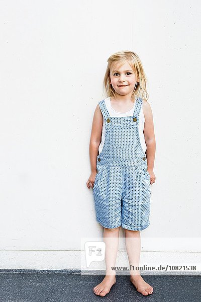 Portrait of girl wearing dungarees in front of white wall