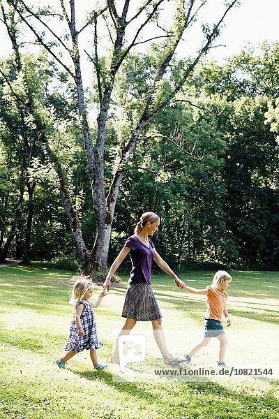 Mid adult woman holding hands with two daughters in park