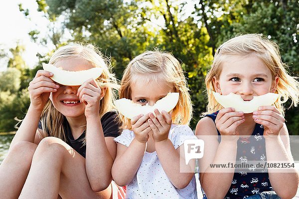 Portrait of three young sisters holding smiling melon in front of face in park
